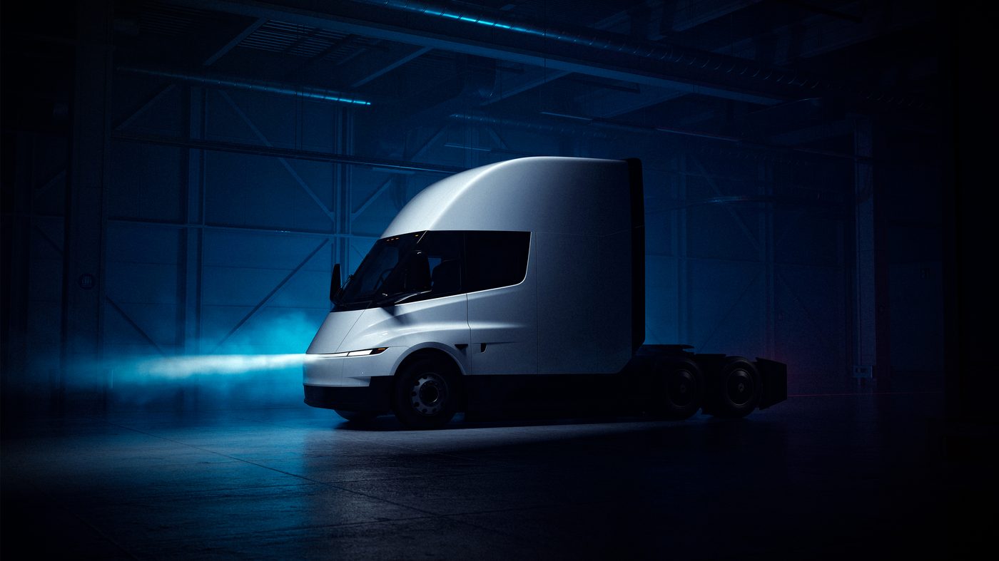 Tesla Semi front three-quarter view in a dark garage with its headlight beam glowing